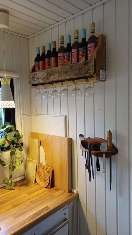 Køkken i sommerhuset på Langeland med vinreol, vin, vinglas, bordplade og køkkenredskaber som skeer, piskeris og skærebrætter.