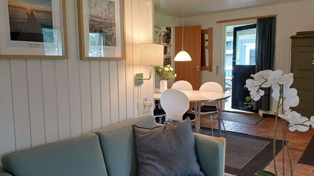 Blå sofa med spisebord i baggrunden, Langelandsfoto på væggen og tændte lamper i sommerhuset på Langeland.