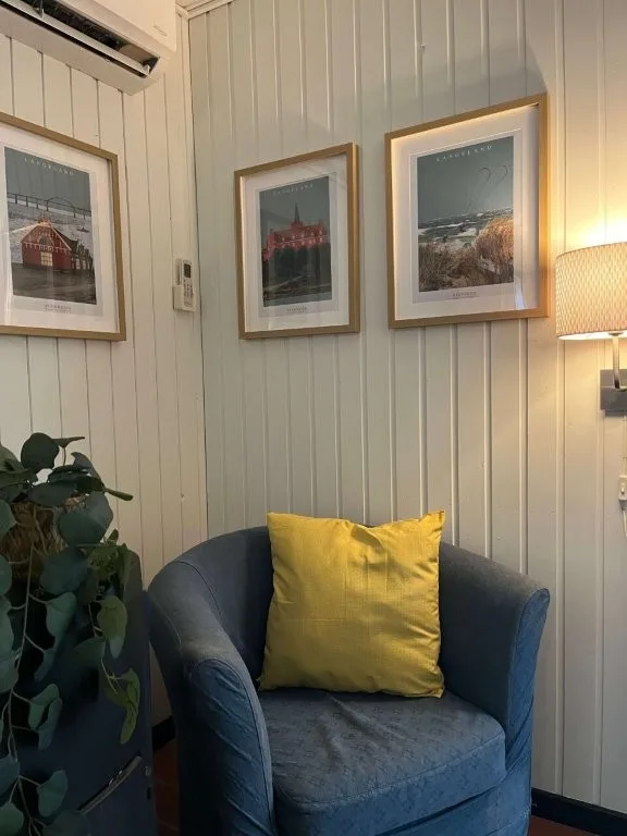 Blå lænestol med gul pude i hyggelig krog med Langelandsfotos på væggen i sommerhuset på Langeland.